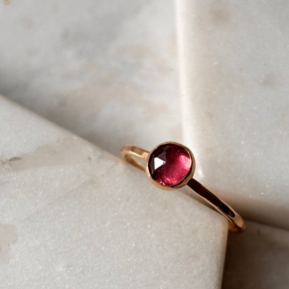 Gold ring with a pink tourmaline gemstone on a marble surface