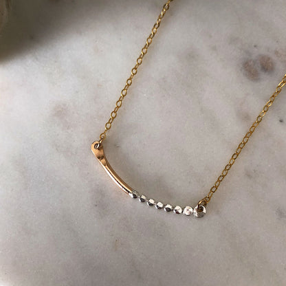 A mixed-metal Prism Bar necklace with a gold-fill chain and silver textured orbs, displayed on a marble surface.