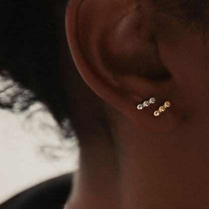 Small textured orb studs in silver and gold, worn in an ear.