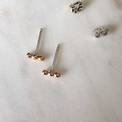 Small textured orb studs in gold, displayed on a marble background.