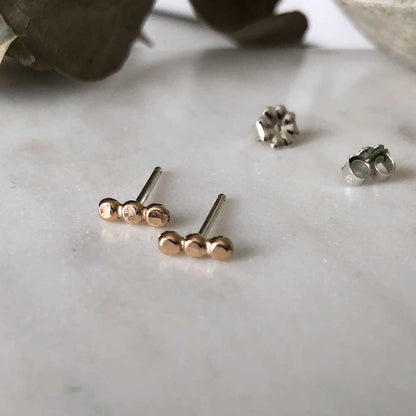 Small textured orb studs in gold, displayed on a marble background.