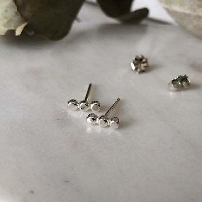 Small textured orb studs in silver, displayed on a marble background.