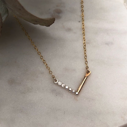 A chevron necklace with a combination of silver and gold-fill metals, featuring a textured pattern on a marble background.