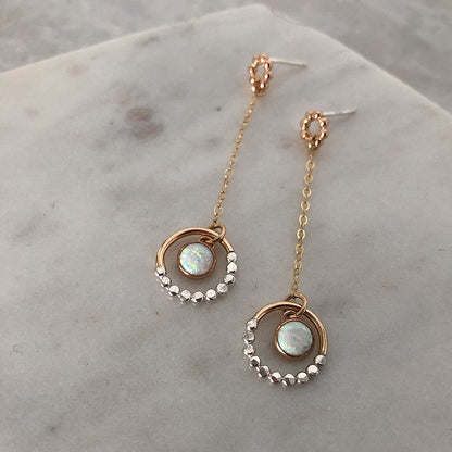 Mixed metal opal dangle earrings on a marble background.