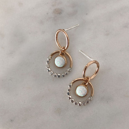 A pair of mixed metal prism gold circle opal drop earrings with sterling silver textures on a marble background.