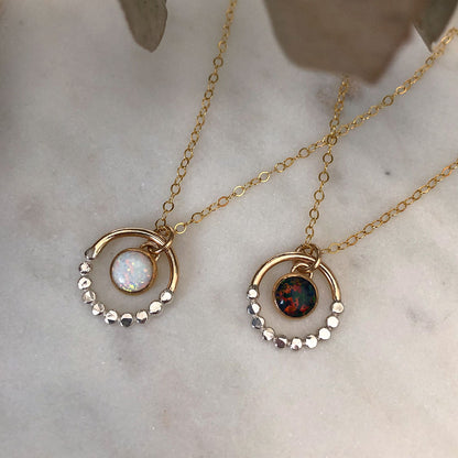 Two opal mixed metal silver and gold textured necklaces, placed on a marble surface.