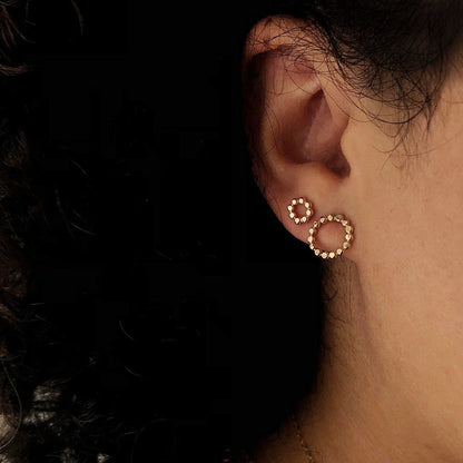 A close-up image of a person wearing a small gold-fill hoop earring with a textured surface.