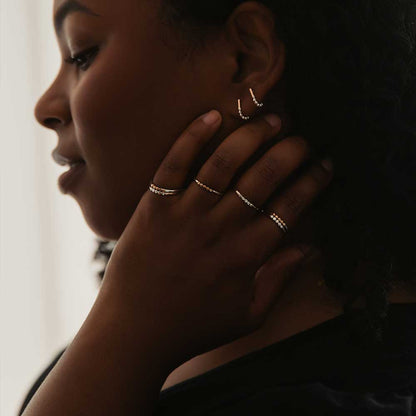 A set of mixed metal earrings and rings worn by a woman with brown skin.