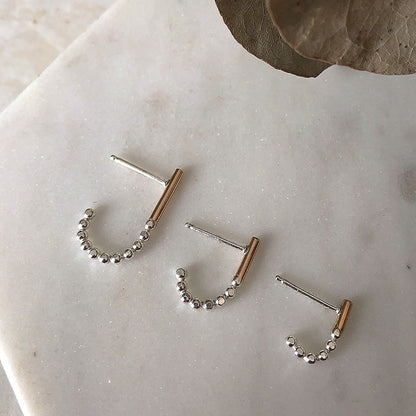 A set of three J-hoop earrings made of sterling silver with hand-textured orbs, displayed on a marble surface.