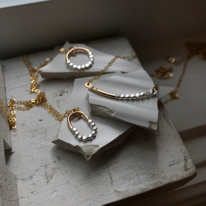 Multiple mixed-metal necklaces with a gold-fill chain and silver textured orbs, displayed on a marble surface.