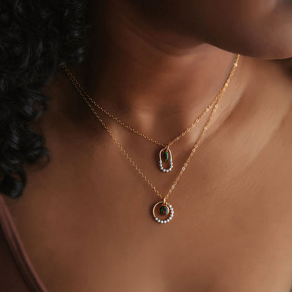 A person with brown skin wearing two black opal mixed metal silver and gold textured necklaces.