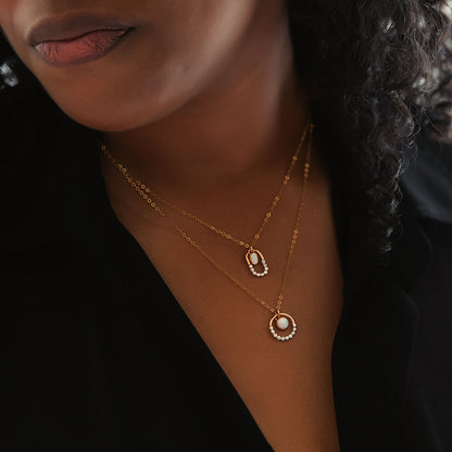 A person with brown skin wearing two opal mixed metal silver and gold textured necklaces.