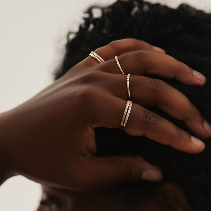 A person wearing rings,  with a gold band and silver orb accents and another with a silver band and gold orb accents.