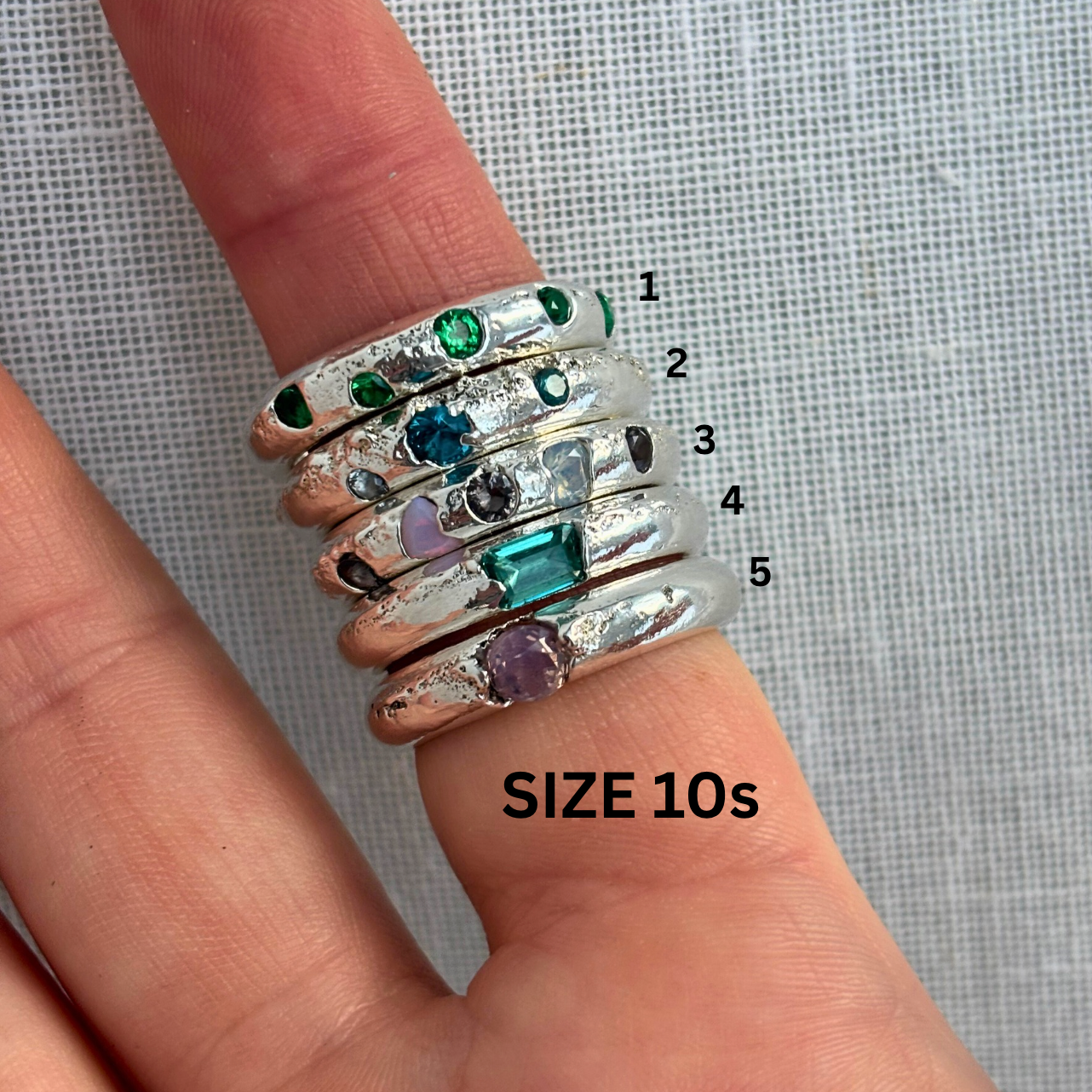 Stack of silver rings with gemstones on a finger, labeled with sizes.