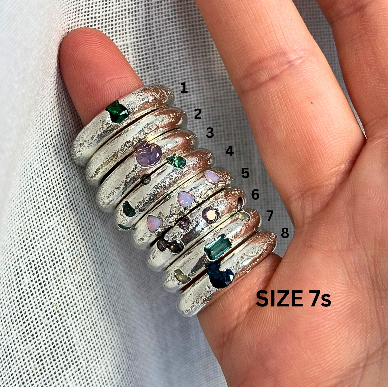 Set of eight silver rings with gemstones on a finger, labeled with size 7.