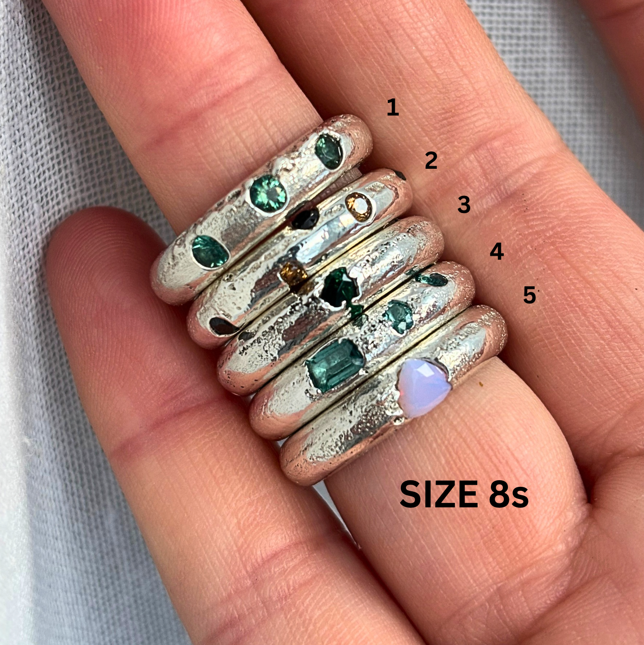 Stack of silver rings with gemstones on a hand, labeled with sizes.