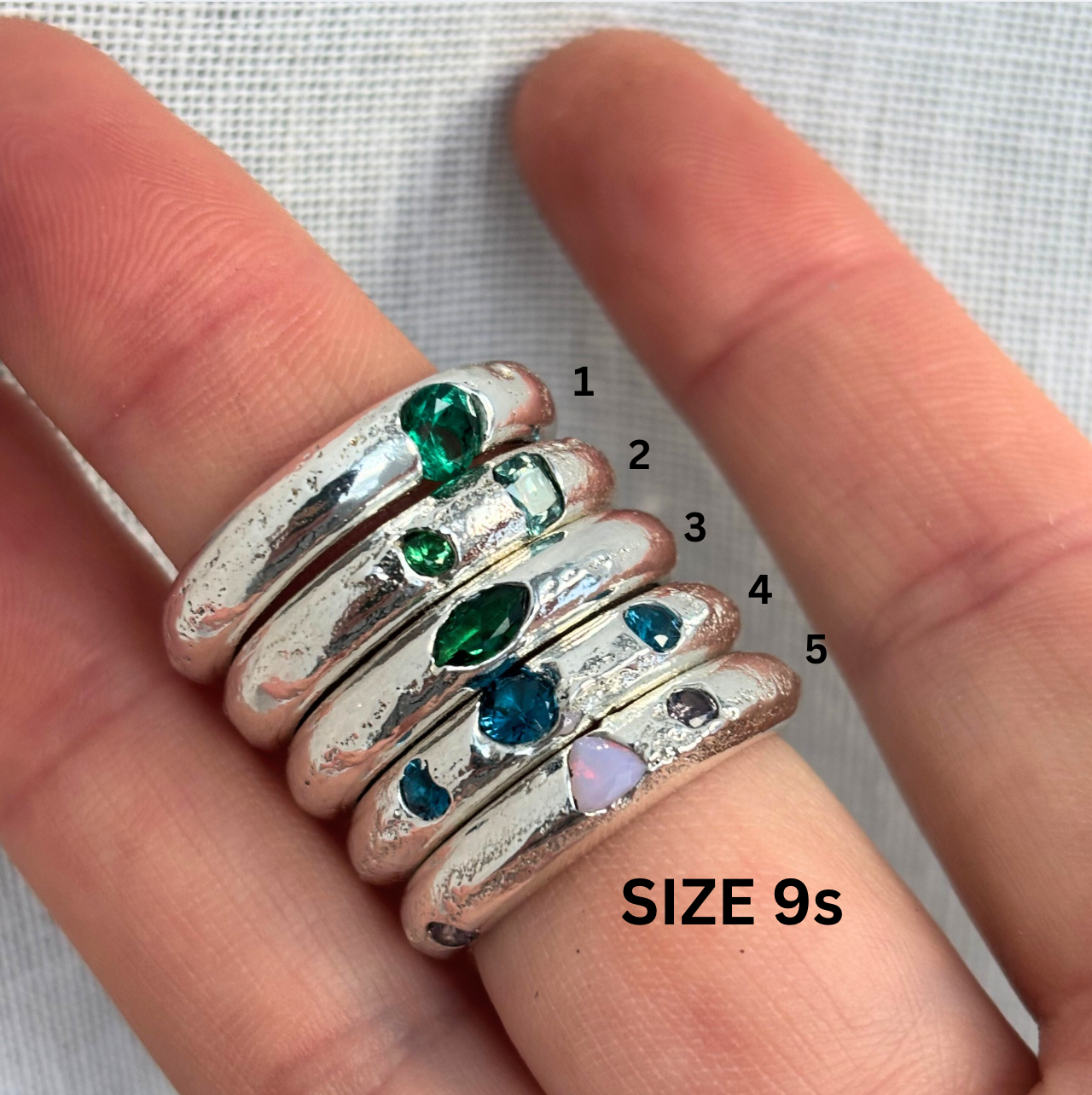 Silver rings with colored gemstones on a finger, labeled with size 9.