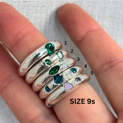 Silver rings with colored gemstones on a finger, labeled with size 9.