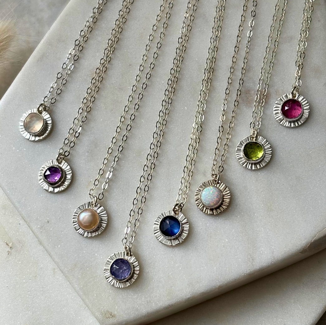 Set of silver necklaces with various coloured gemstones on a marble surface
