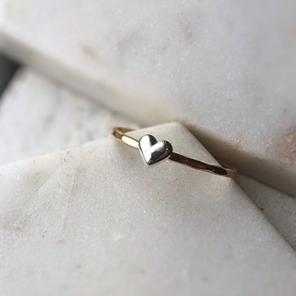 A gold-filled ring with a sterling silver heart on a marble surface.