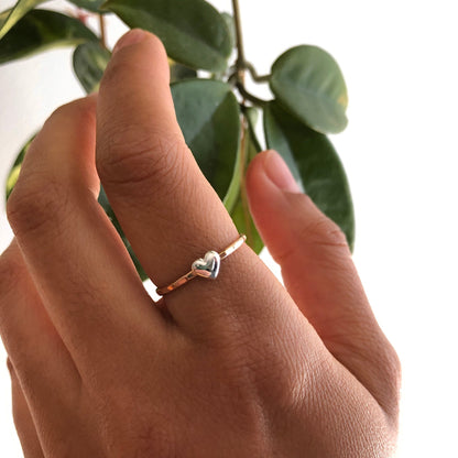 A hand wearing a gold-filled ring with a sterling silver heart with a leaf in the background.