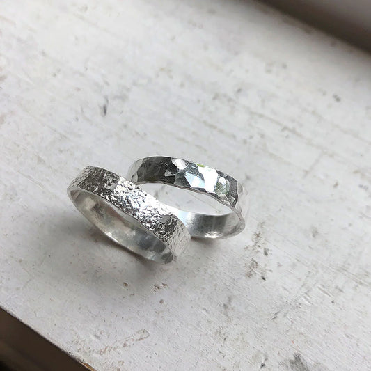 Two silver rings with textured surfaces on a light gray surface
