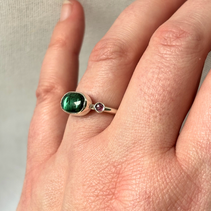 Ring with a green gemstone on a finger against a neutral background