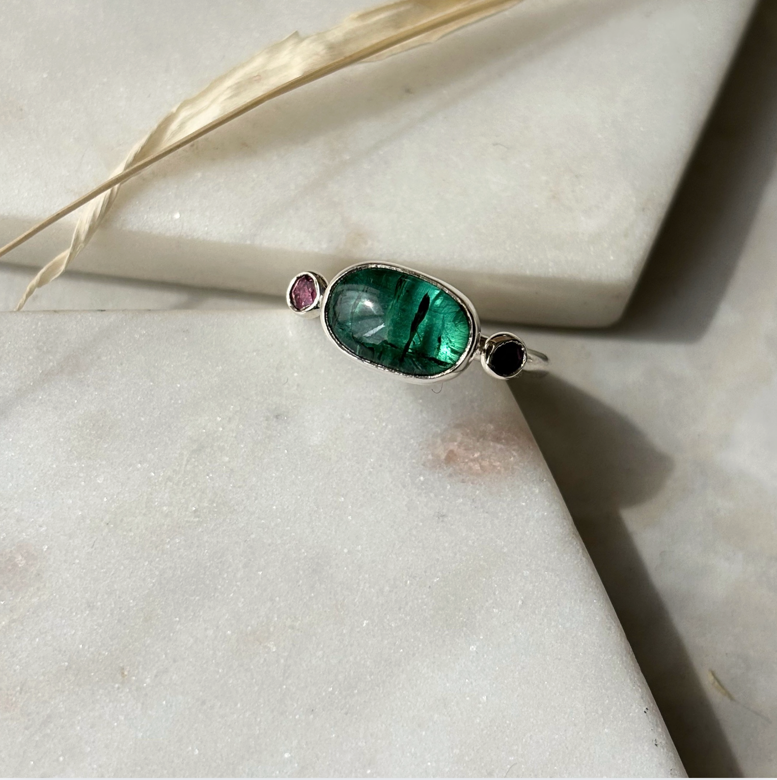 Silver ring with a green gemstone on a light stone surface