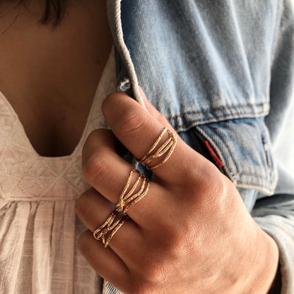 A hand with multiple gold rings on a neutral background