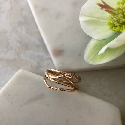 A gold ring with multiple criss crossing wires on a neutral background.