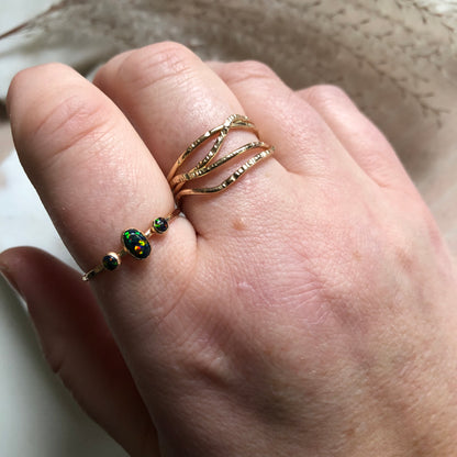 A hand wearing a gold ring with multiple criss crossing wires on a neutral background.
