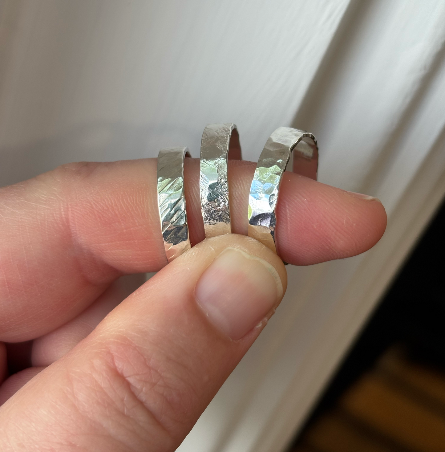 Three silver rings being held between fingers against a white background