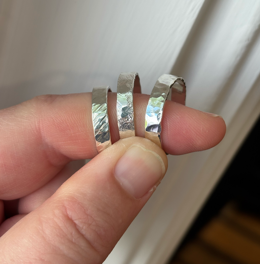 Three silver rings being held between fingers against a white background