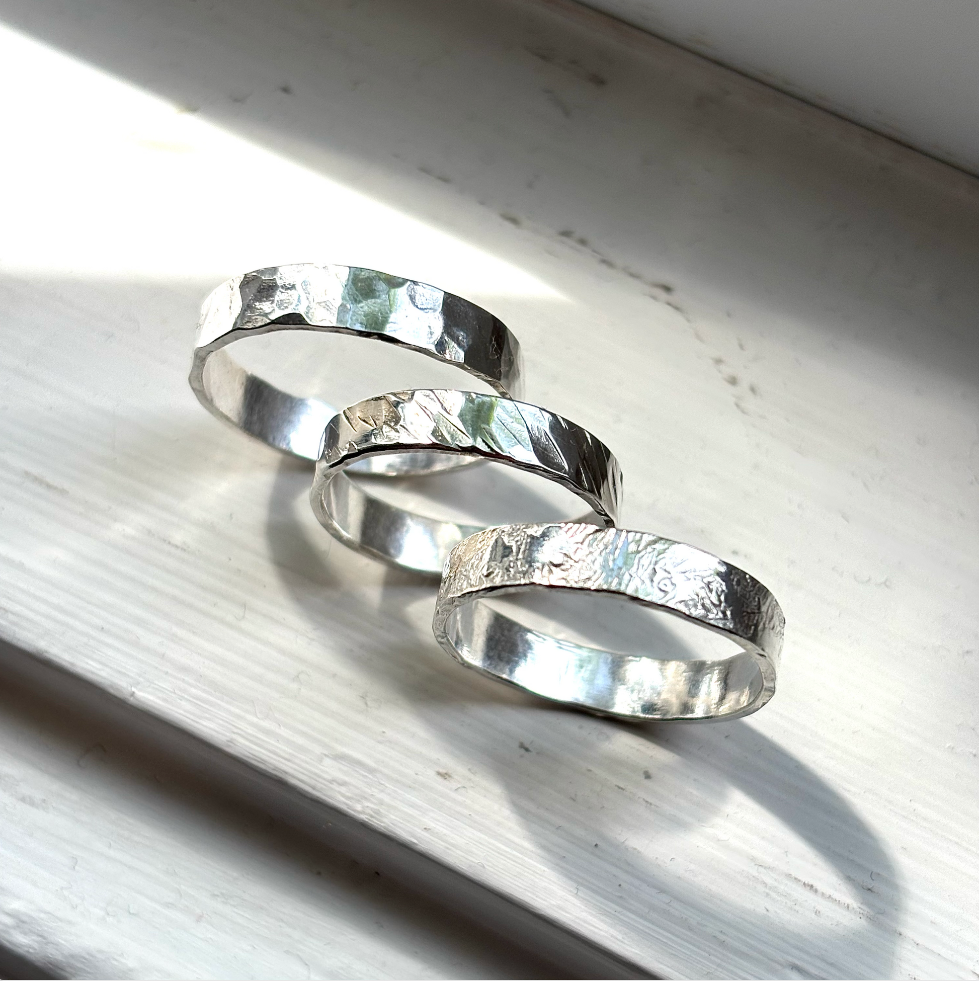 Three silver rings with textured surfaces on a light wooden surface.