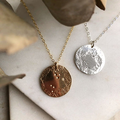 Two zodiac pendant necklaces, one with a gold-fill pendant and the other with a silver pendant, both on a cable chain, displayed against a neutral background.