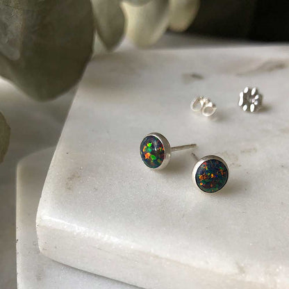 A pair of black opal stud earrings on a marble surface, with a blurred background.