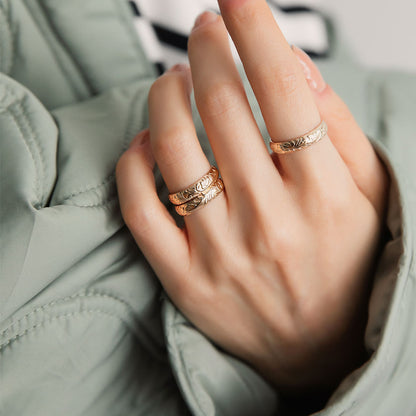 A person wearing three gold floral motif band rings.
