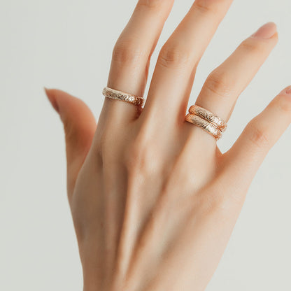 A person wearing three gold floral motif band rings.