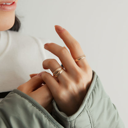 A person wearing three gold floral motif band rings.